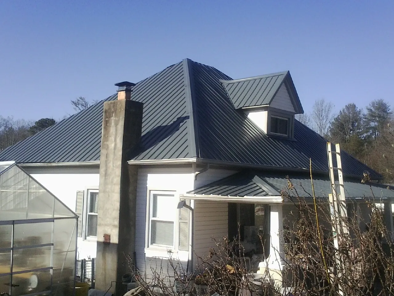 Dark blue standing seam metal roof on a white farmhouse with dormer — Slate & Tile Roof Repair by Roofing Brothers in Rock River