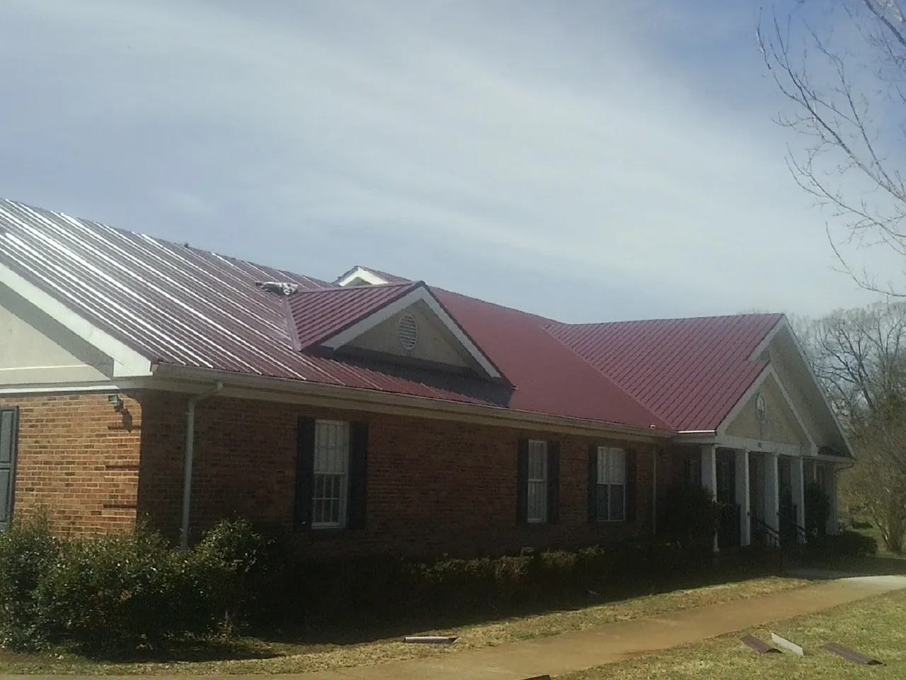Red metal roof with gabled entries on a long brick building, from a Hail Damage Roof Repair job in Rock River