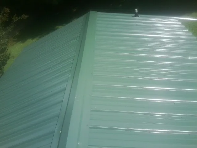 New green metal panels meeting at the ridge of a roof — Flat Roof Repair work by our crew in Rock River