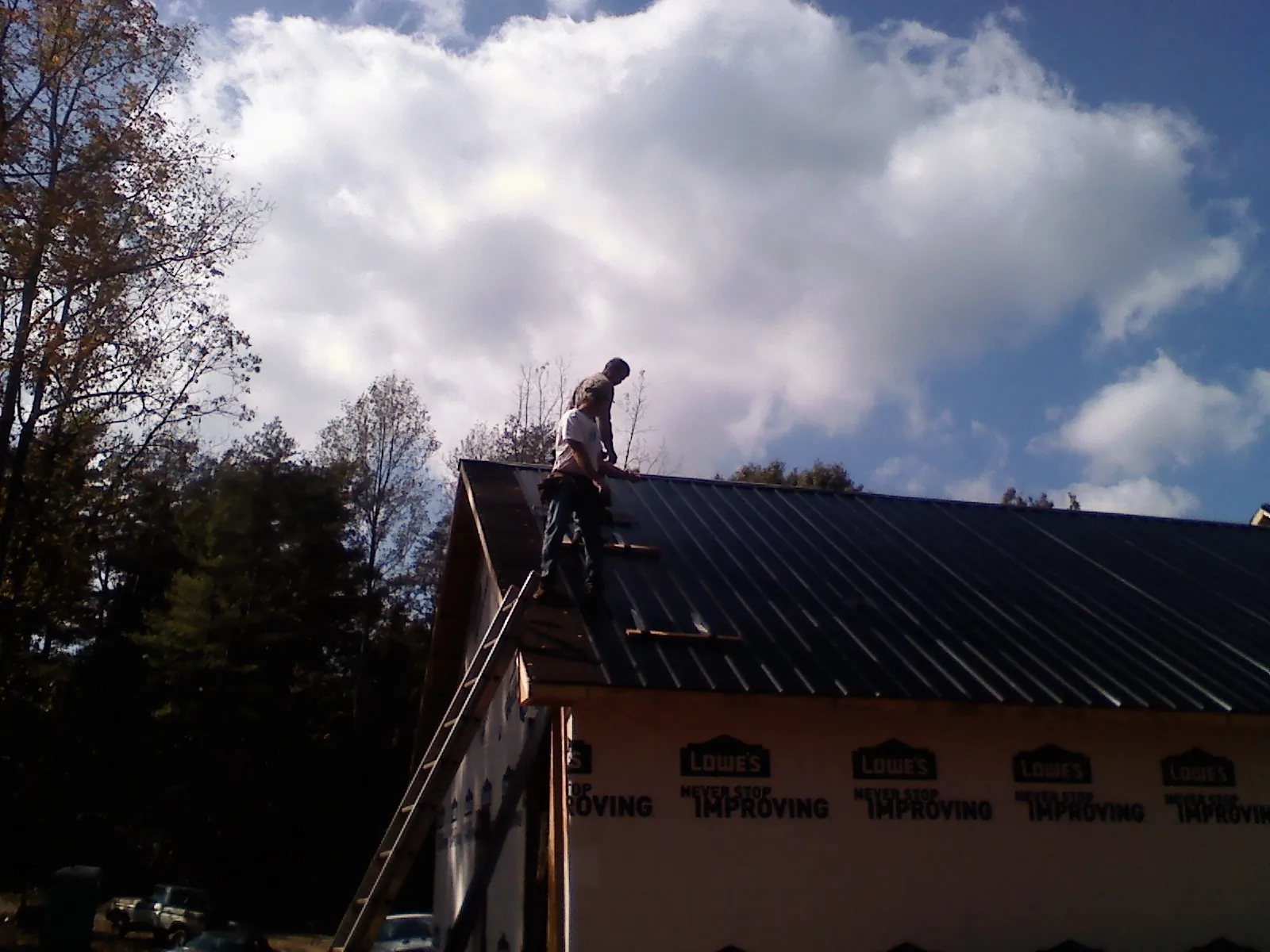 Roofer fastening dark metal panels high against a cloudy sky, from a Roof Inspection job in Rock River