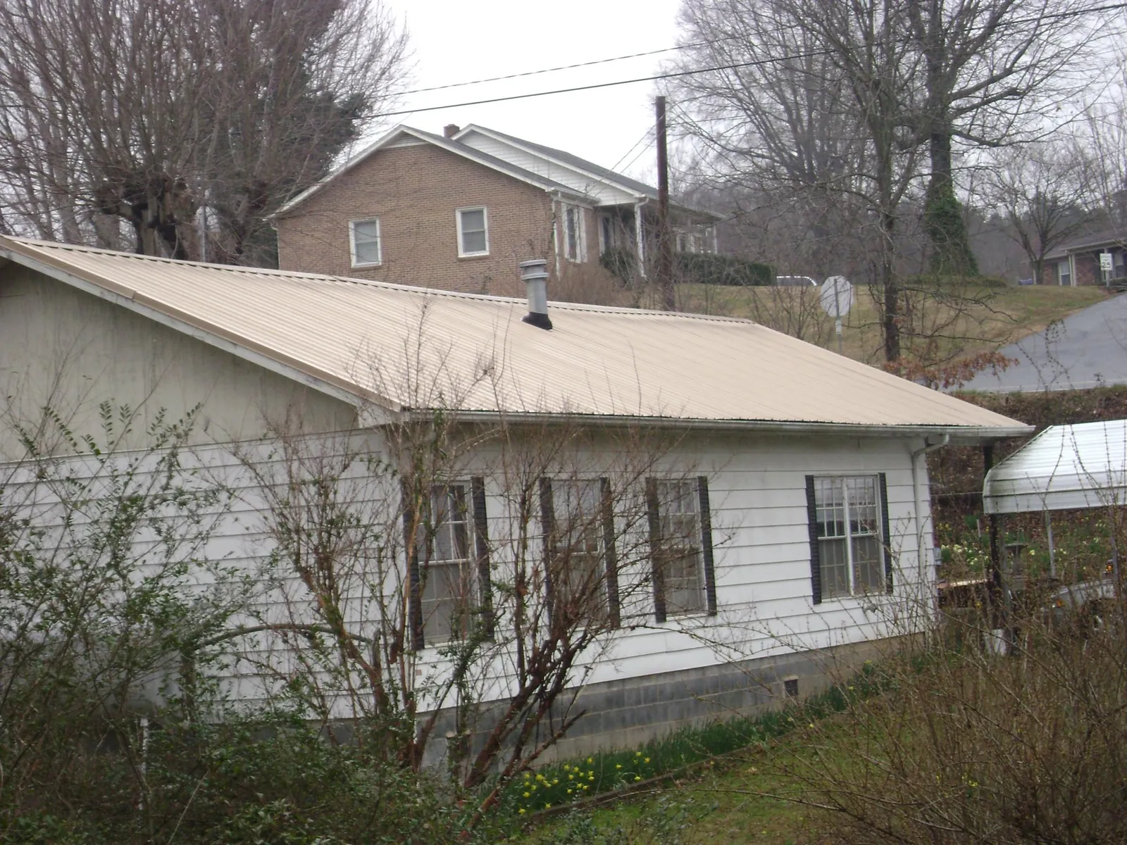 Tan metal roof on a white sided house set into a hillside — Commercial Roofing by Roofing Brothers in Rock River