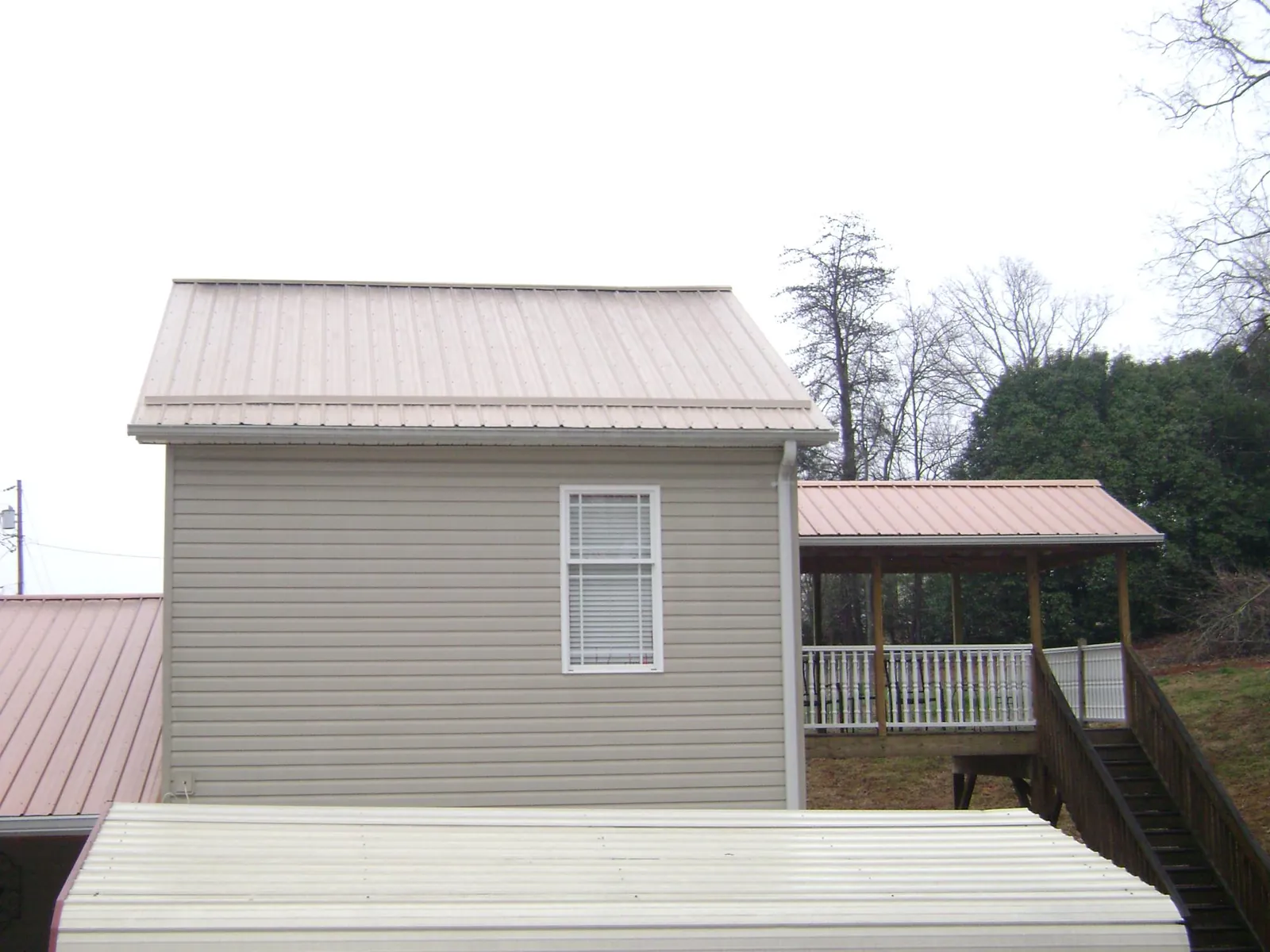 Tan metal roofs on a two story addition and attached porch, from a Roof Replacement job in Rock River